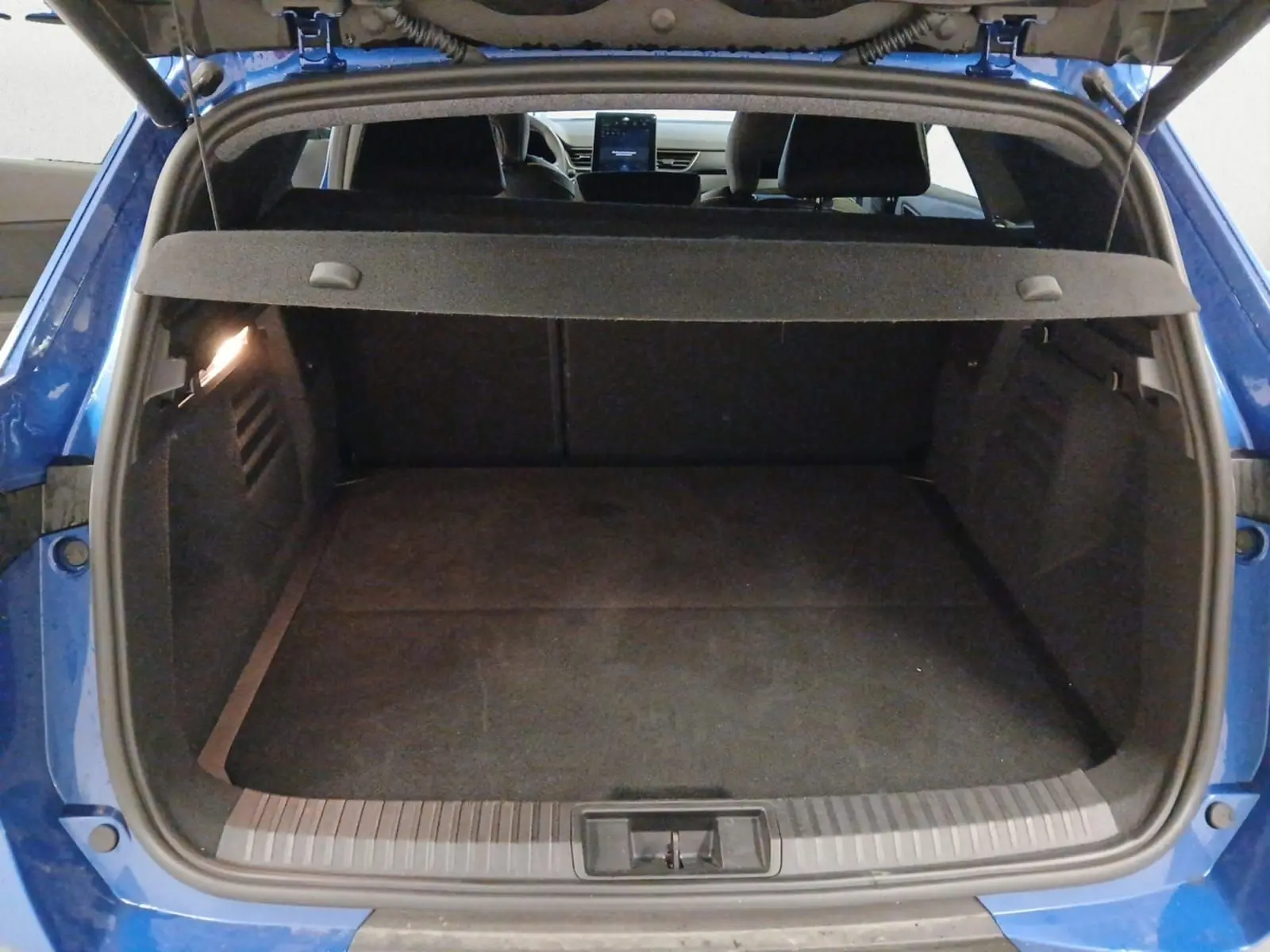 Coffre ouvert vu de l'arrière d'une Renault Symbioz bleu iron, montrant l'espace de chargement et la tablette arrière.