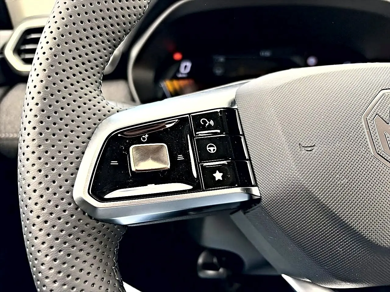 Gros plan sur la partie gauche du volant perforé gris du MG Motor ZS 1.5 hybrid 197 avec commandes intégrées.