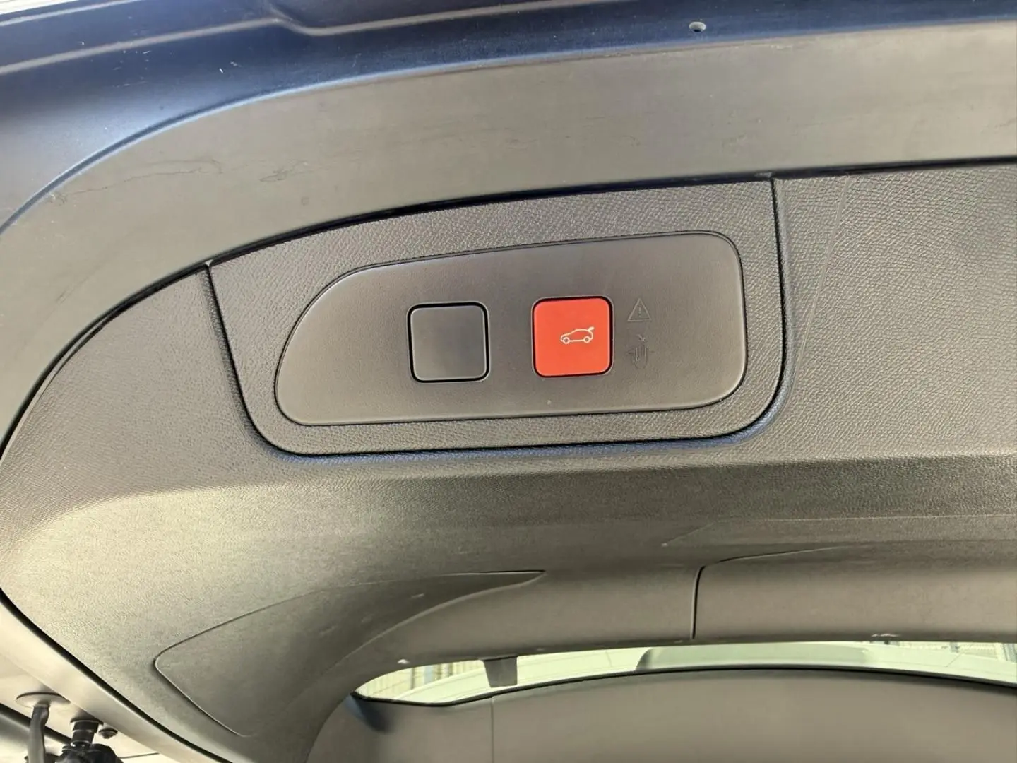 Gros plan sur le bouton d'ouverture du coffre rouge à l'intérieur du hayon du DS7 gris métal 2025.