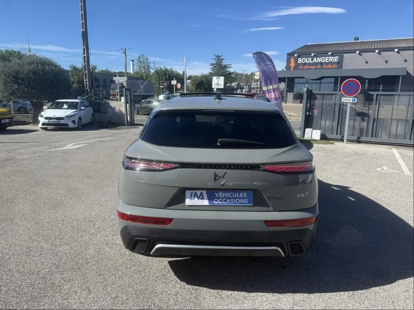 Vue arrière d’un DS7 gris métal 2025 avec feux allongés et logo DS distinctif, stationné devant une boulangerie.