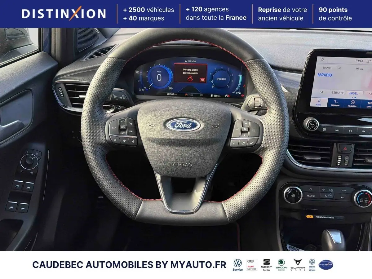 Vue intérieure centrée sur le volant perforé avec surpiqûres rouges et tableau de bord numérique du Ford Puma 2024.