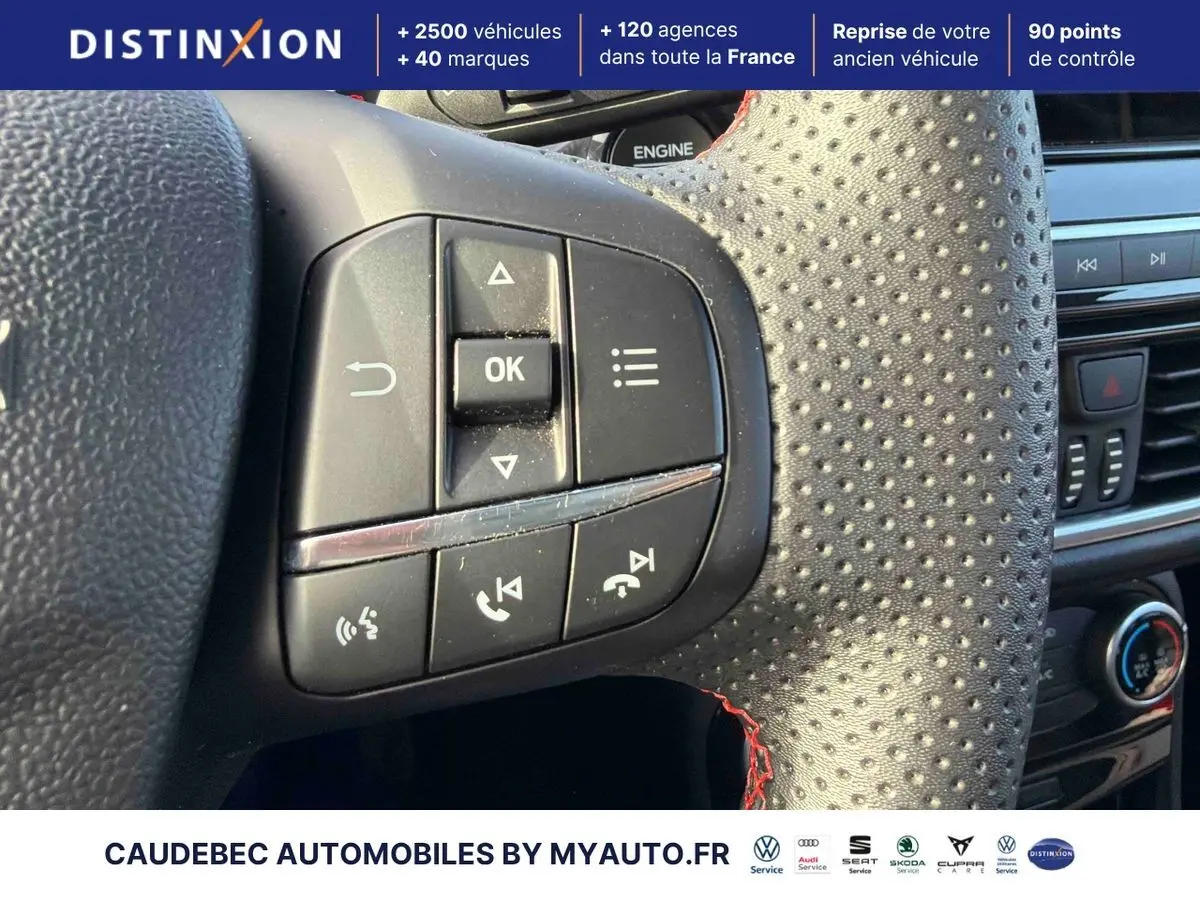 Gros plan sur les commandes multifonctions à gauche du volant perforé avec surpiqûres rouges du Ford Puma bleu.