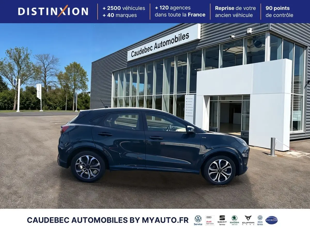 Ford Puma bleu en profil droit, avec jantes alliage 17 pouces et badges ST-Line visibles, devant un showroom.