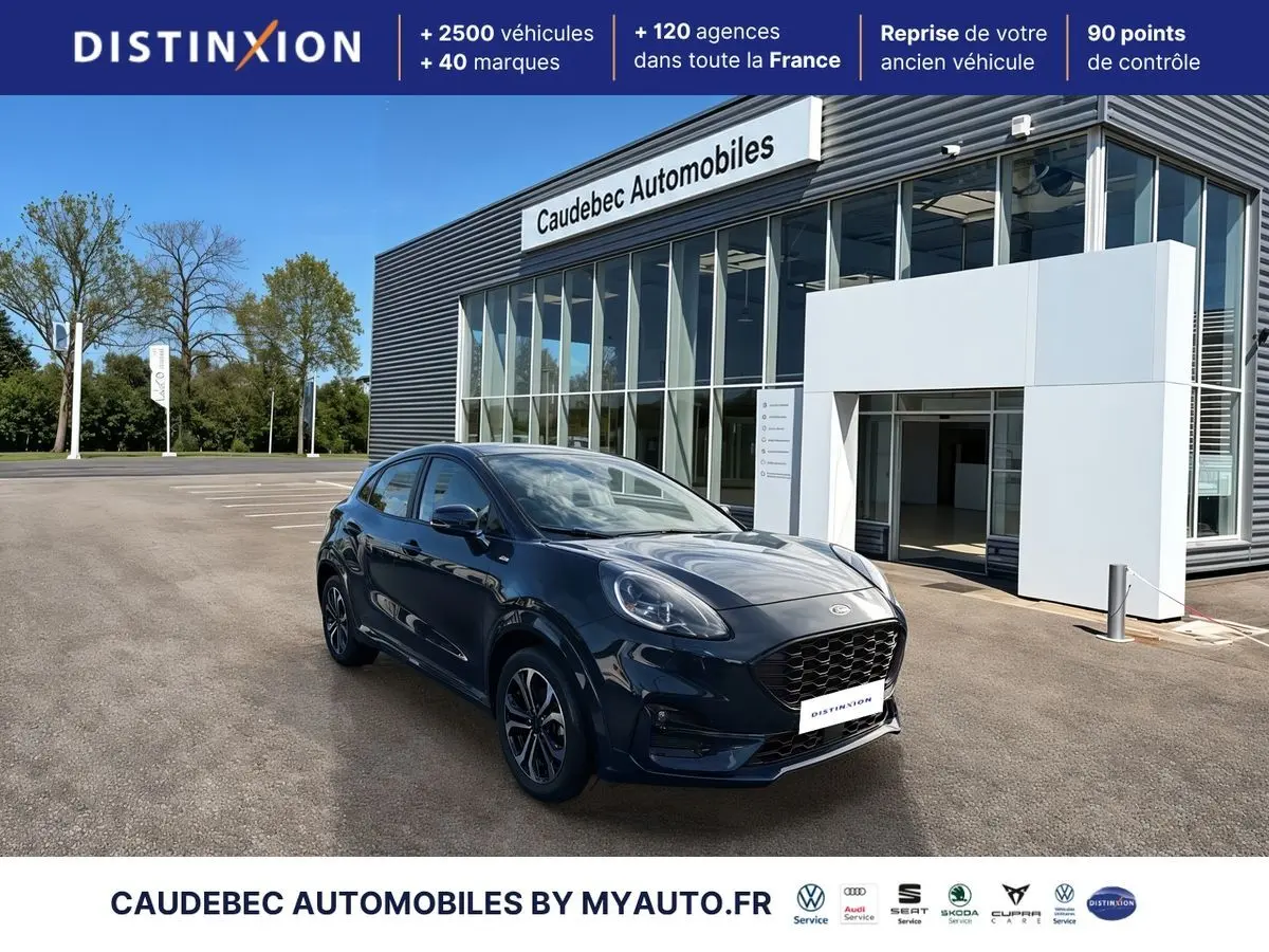 Ford Puma bleu foncé en 3/4 avant droit, avec jantes alliage 17 pouces et calandre noire, devant un showroom.