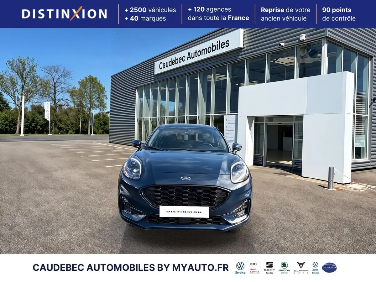 Vue avant d'une Ford Puma bleue 2024 avec calandre noire et phares LED, devant un showroom moderne.