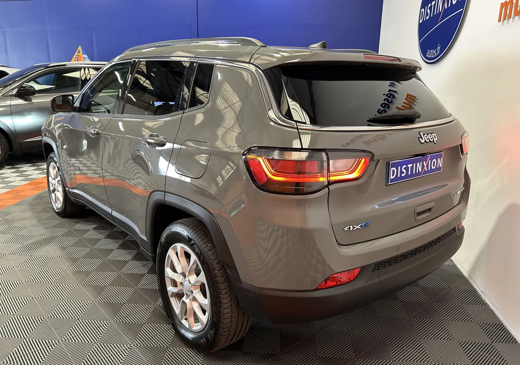 Vue 3/4 arrière droite d'un Jeep Compass gris 2021 avec feux allumés et badge 4xe en concession