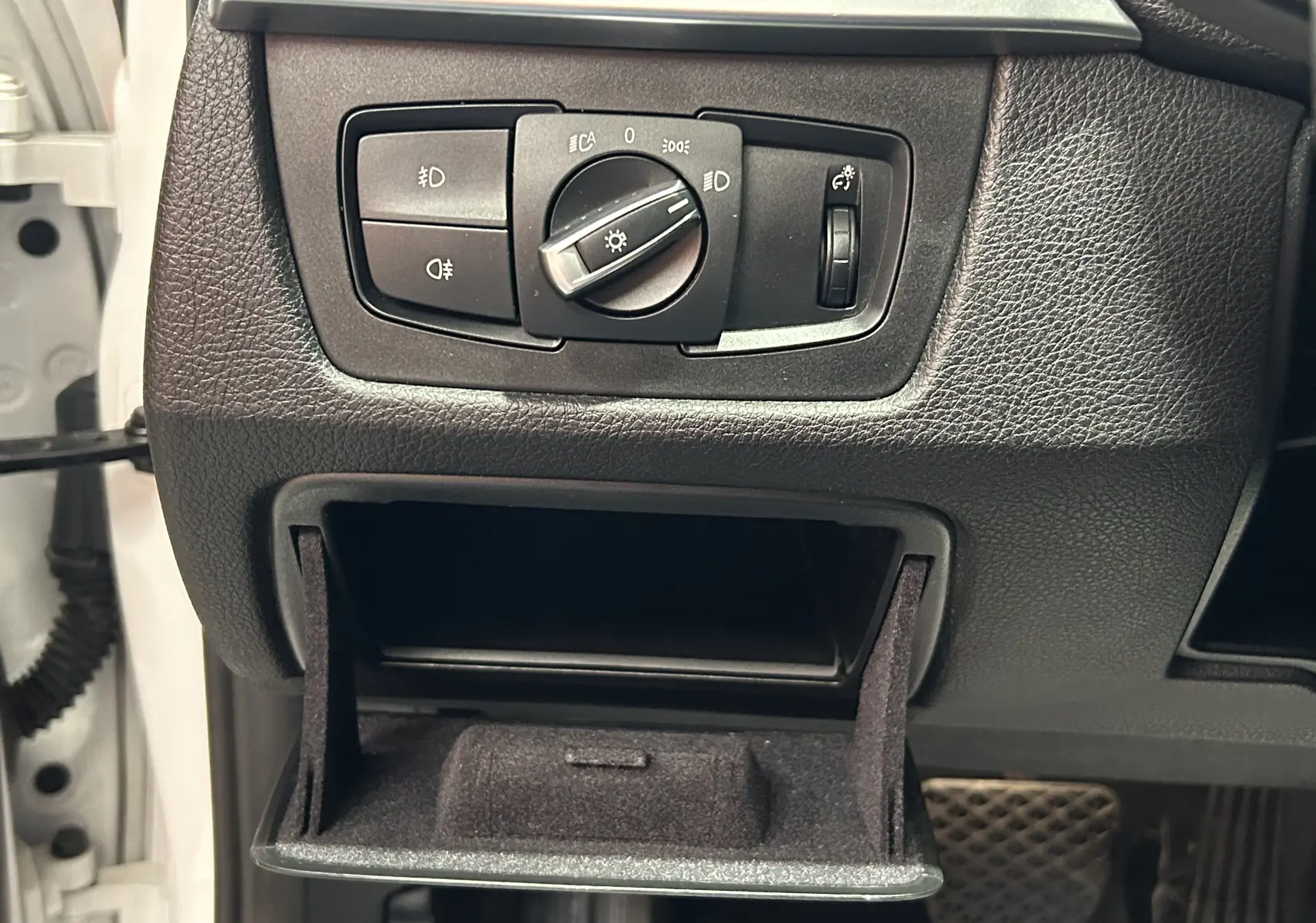 Gros plan sur le tableau de bord noir de la BMW Série 3 320i 2018, avec commande d'éclairage et rangement ouvert.