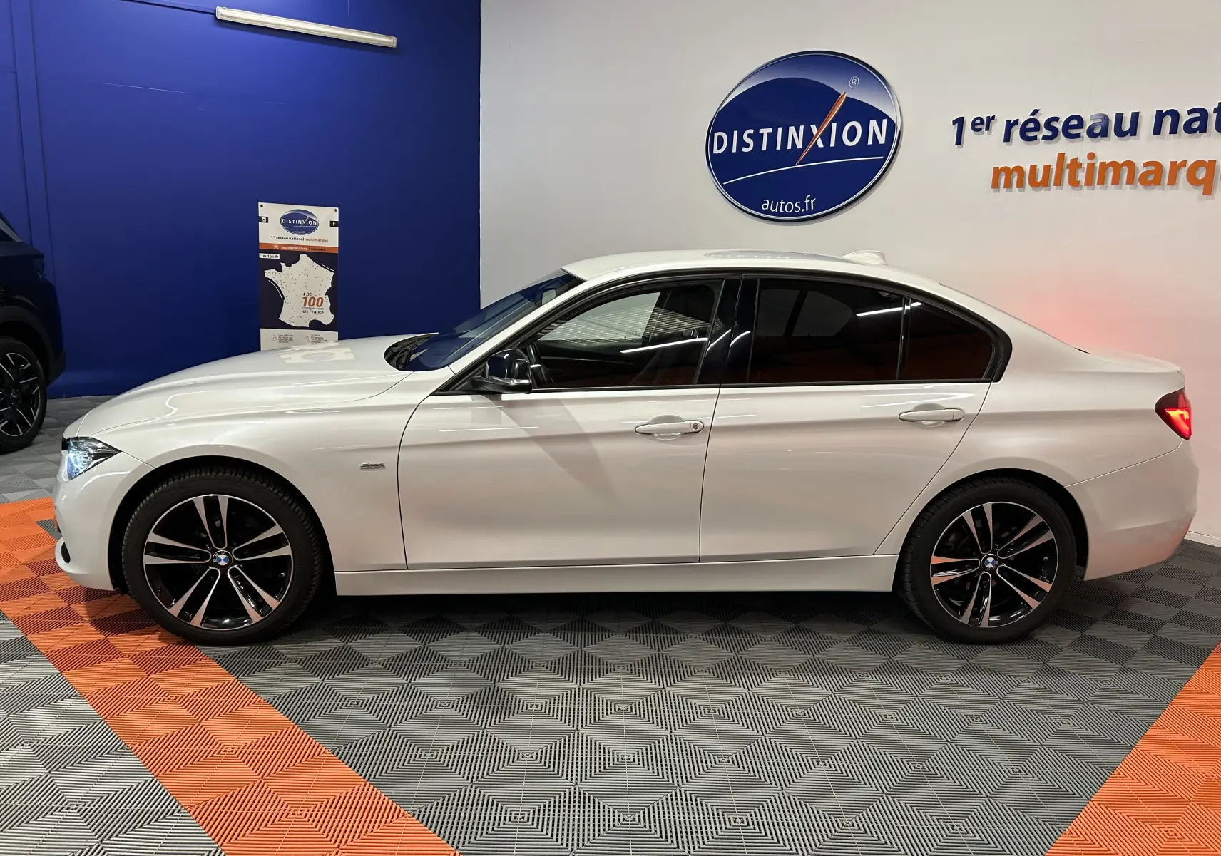 BMW Série 3 320i blanc vue de profil côté gauche, avec jantes noires et vitres teintées en intérieur showroom.
