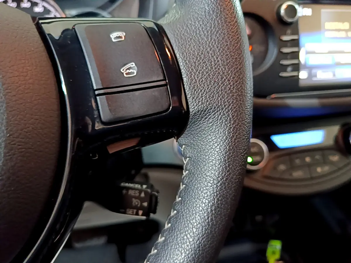 Gros plan sur le volant cuir noir de la Toyota Yaris hybride 2020 avec commandes intégrées et tableau de bord flou en arrière-plan