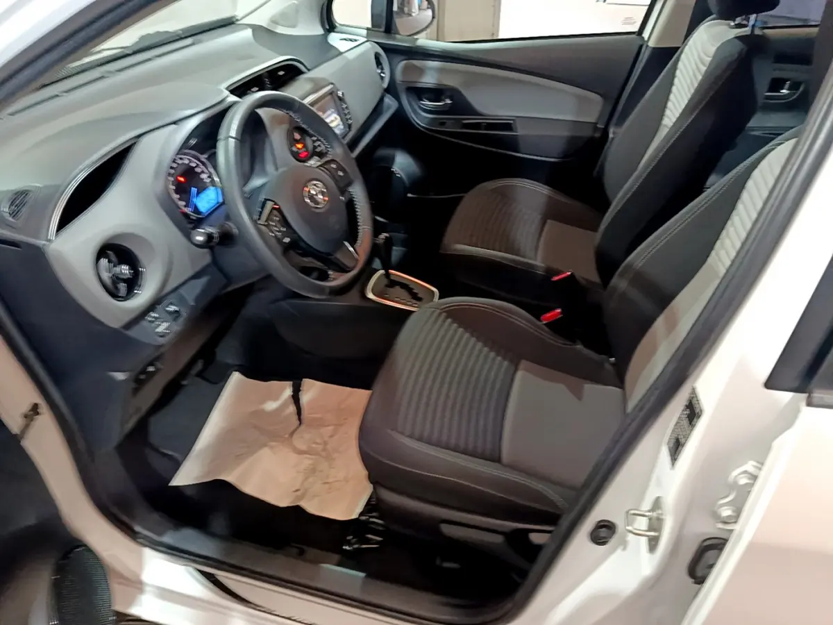Intérieur avant gauche d'une Toyota Yaris blanche 2020, sièges tissu noirs et tableau de bord avec écran tactile.