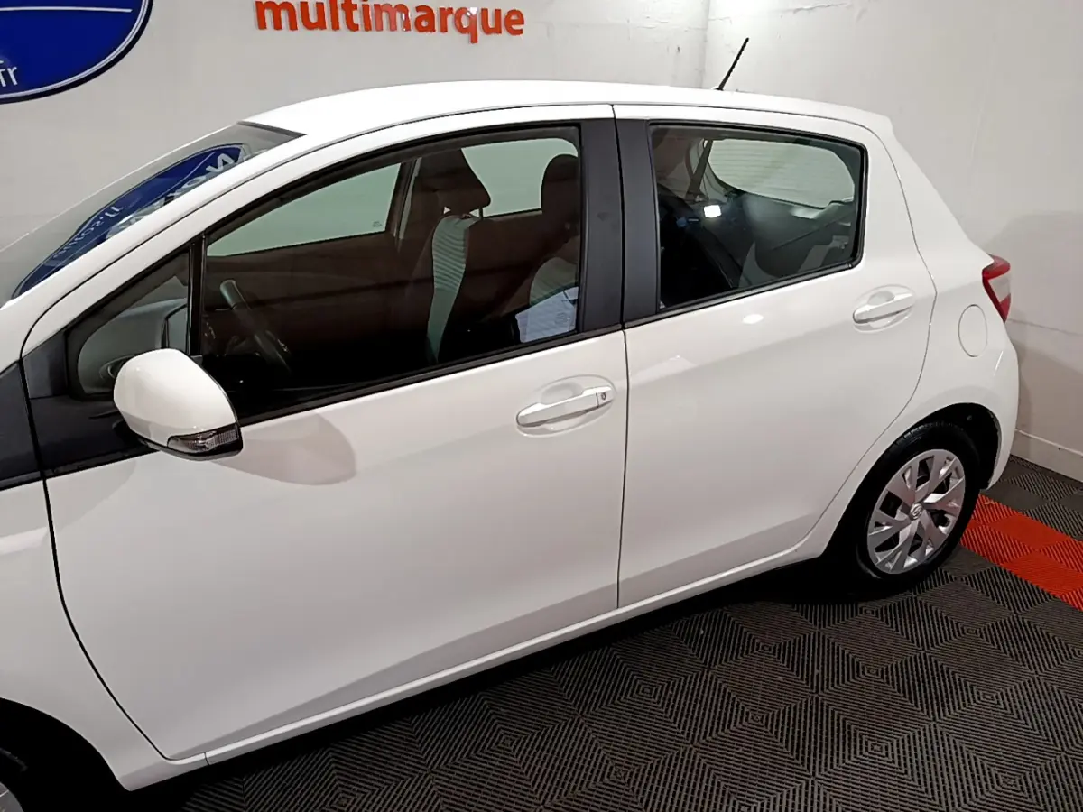 Profil côté gauche d'une Toyota Yaris blanche 2020, version hybride, avec rétroviseur et jantes visibles.
