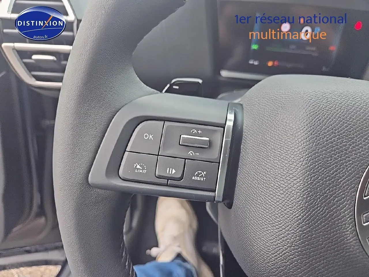 Gros plan sur les commandes au volant cuir noir de la Citroën C4 1.2 hybride 2025, avec tableau de bord numérique en arrière-plan.