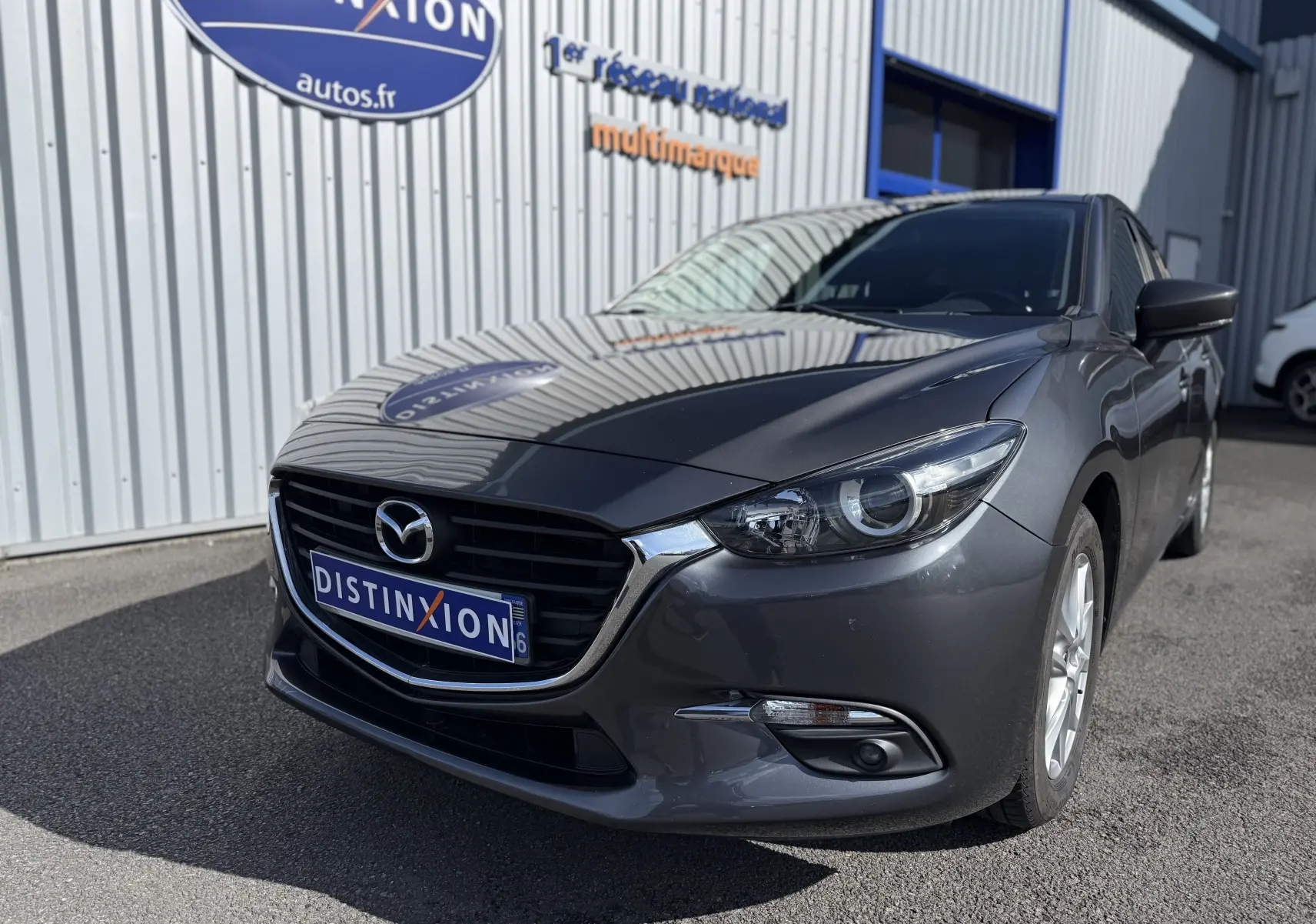Vue 3/4 avant droite d'une Mazda3 gris métallisé 2017 avec calandre noire et phares LED visibles.