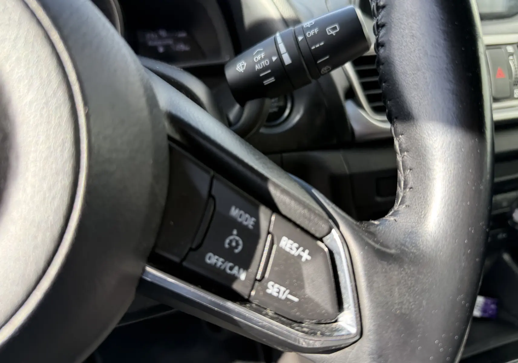 Gros plan sur les commandes du régulateur de vitesse au volant en cuir noir de la Mazda3 gris 2017.