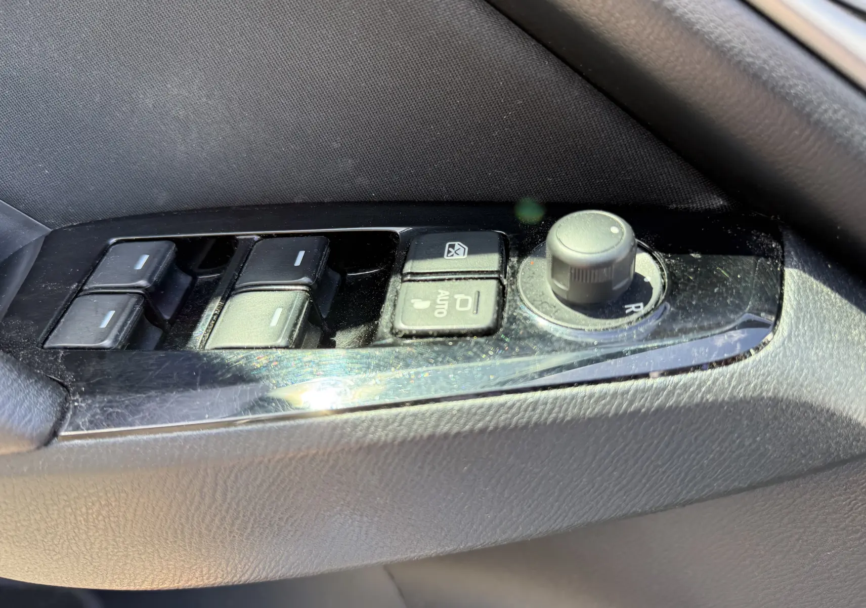 Gros plan sur les commandes de lève-vitres et réglage des rétroviseurs côté gauche d’une Mazda3 gris 2017.