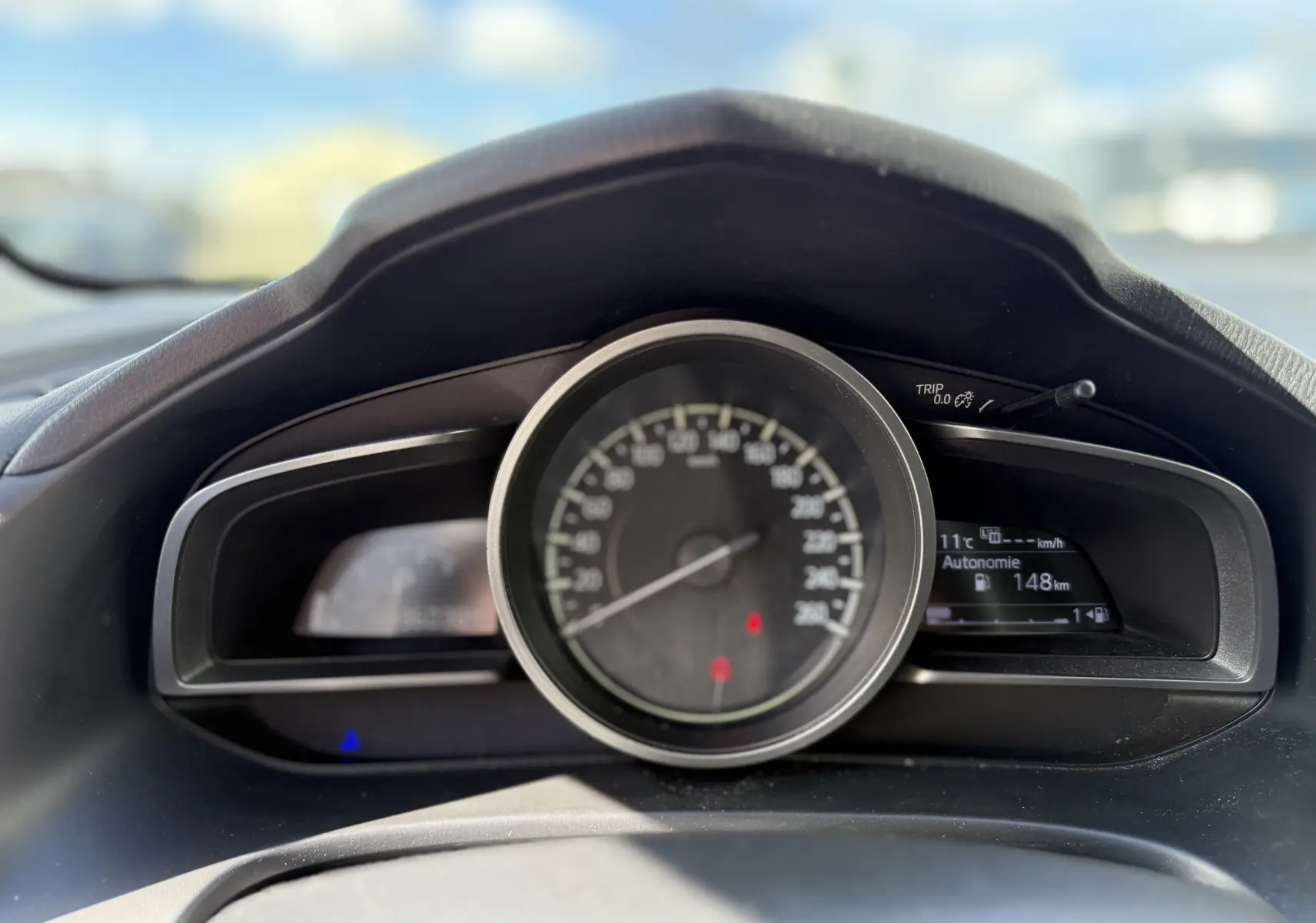 Vue rapprochée du tableau de bord de la Mazda3 gris 2017, affichant la vitesse et l'autonomie de 148 km.