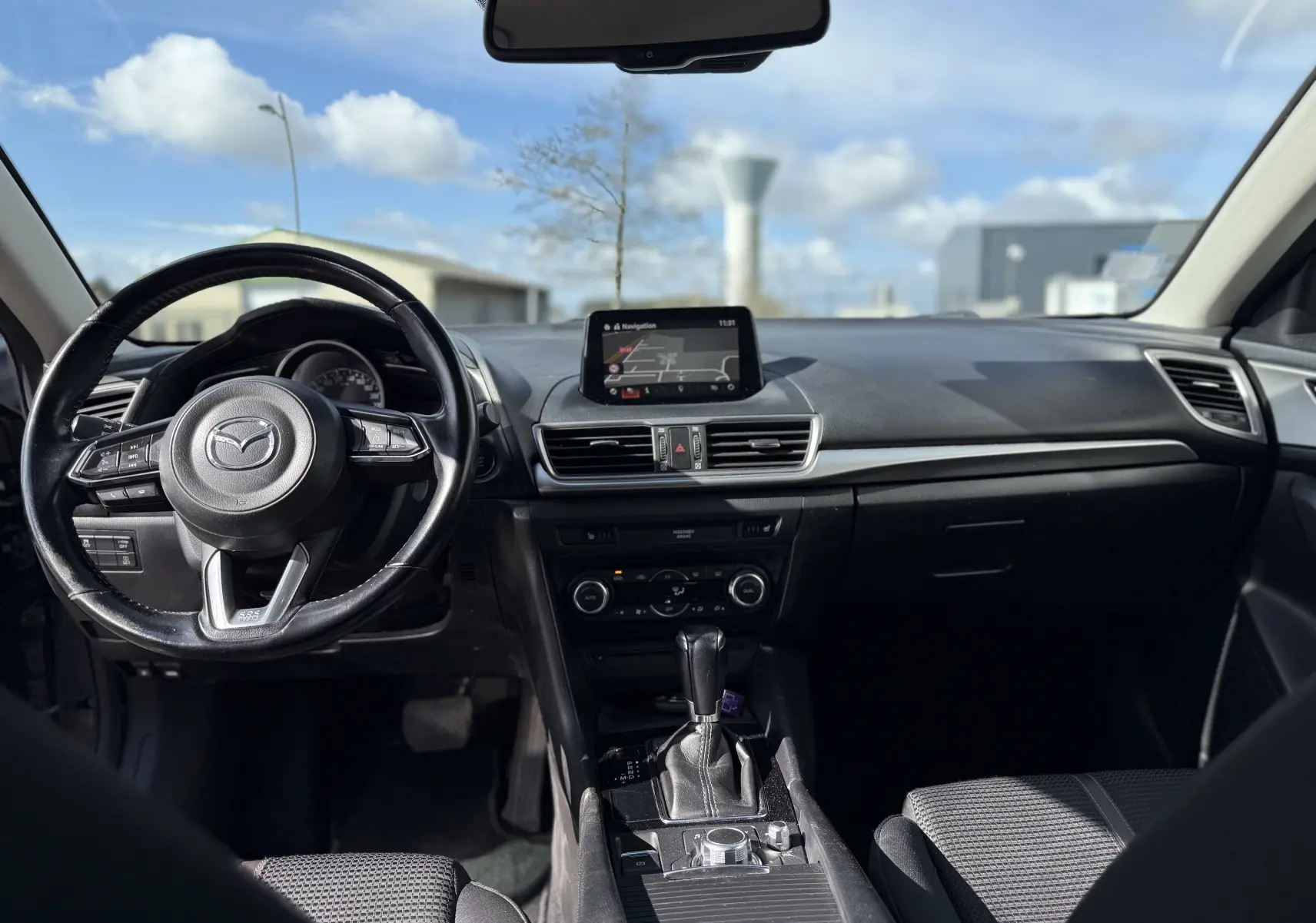 Vue intérieure avant de la Mazda3 2017 avec tableau de bord noir, volant multifonction et écran central de navigation.