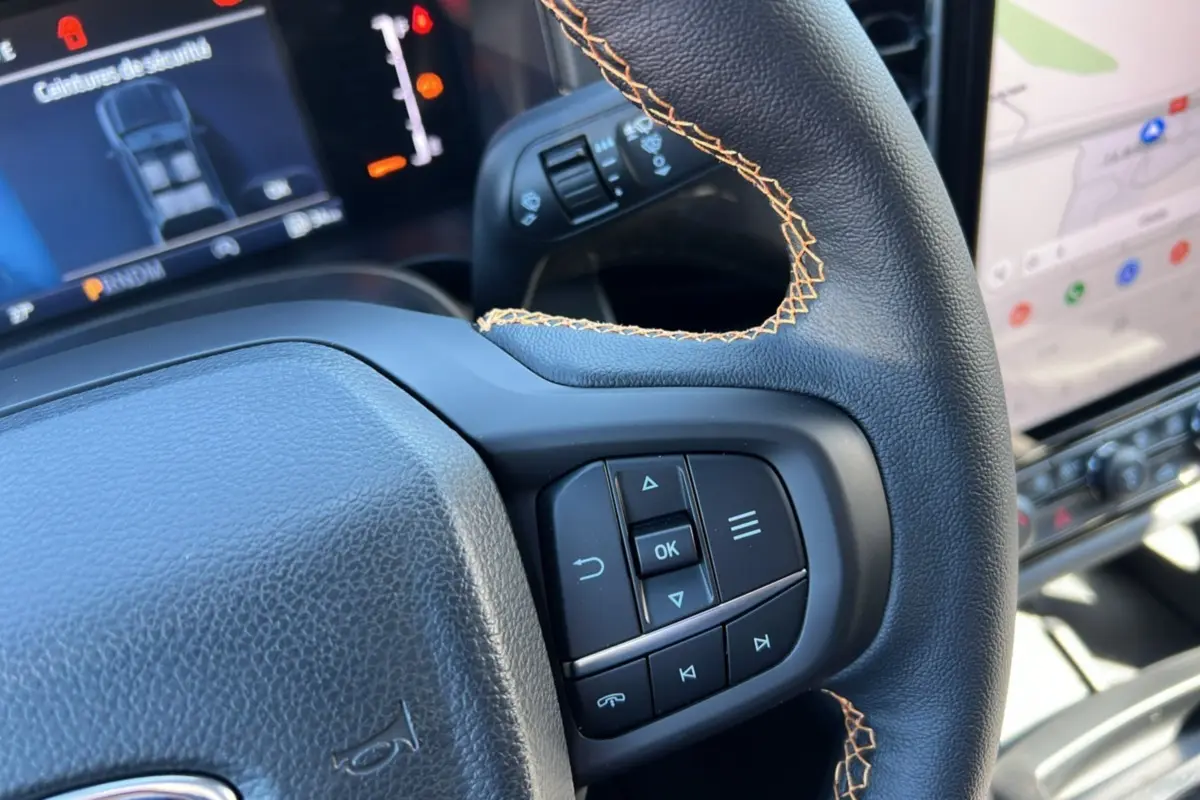 Gros plan sur le volant cuir noir avec surpiqûres orange du Ford Ranger Wildtrak 2025, écran tactile en arrière-plan.