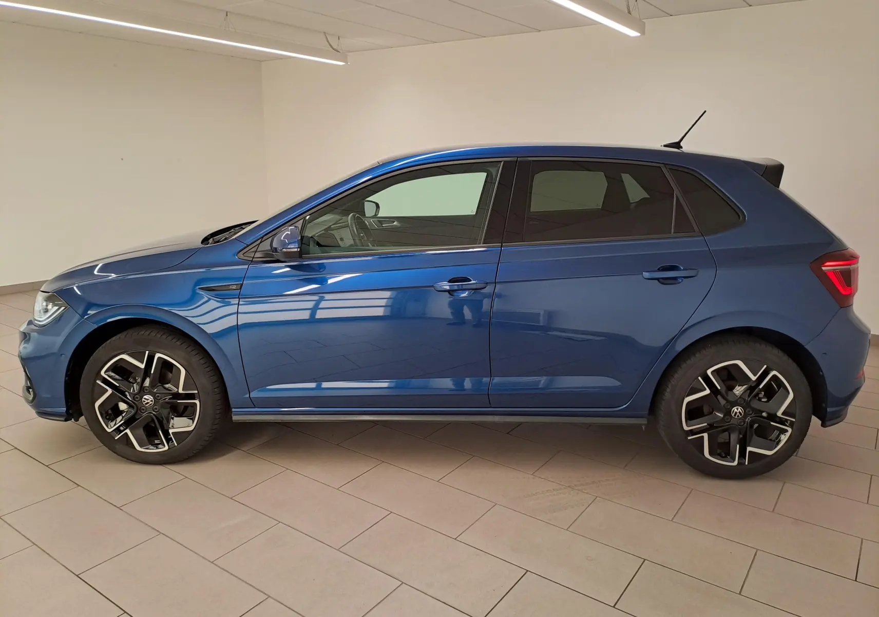 Profil droit d'une Volkswagen Polo 1.0 TSI R-Line Edition 2025 en bleu récif métallisé, avec jantes distinctives noires et argent.