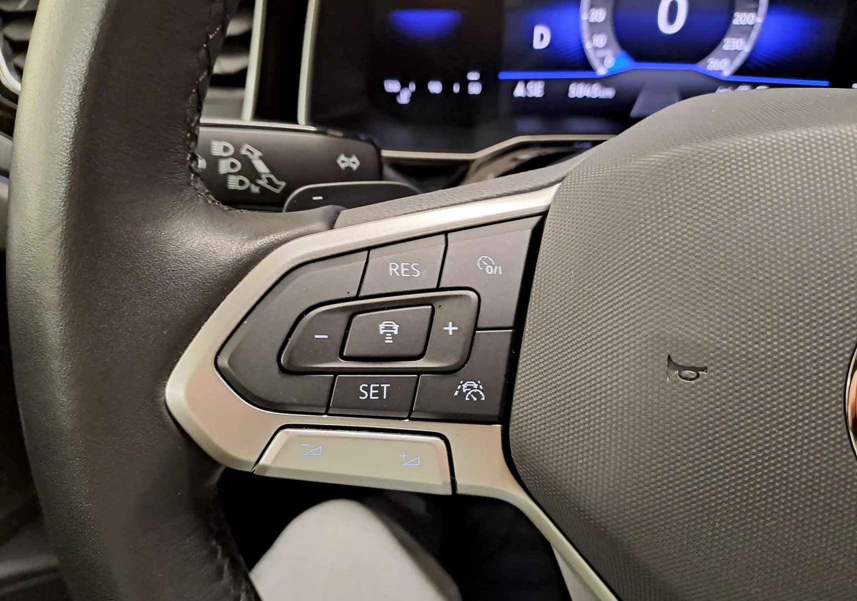 Gros plan sur les commandes à gauche du volant noir de la Volkswagen Polo Bleu Récif, affichage digital en arrière-plan.