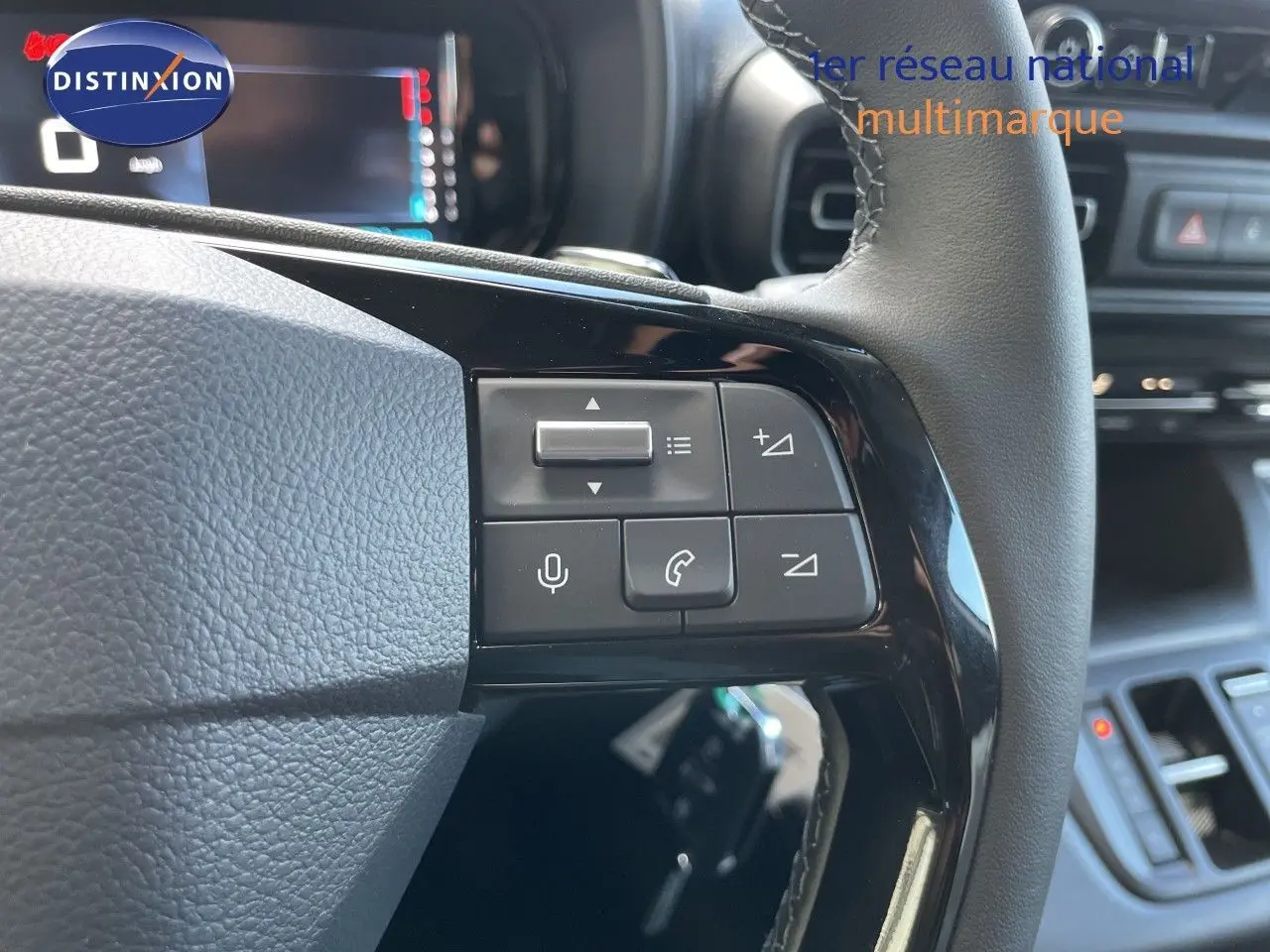 Gros plan sur les commandes au volant en cuir noir du Citroën Berlingo 2026, avec tableau de bord numérique en arrière-plan.