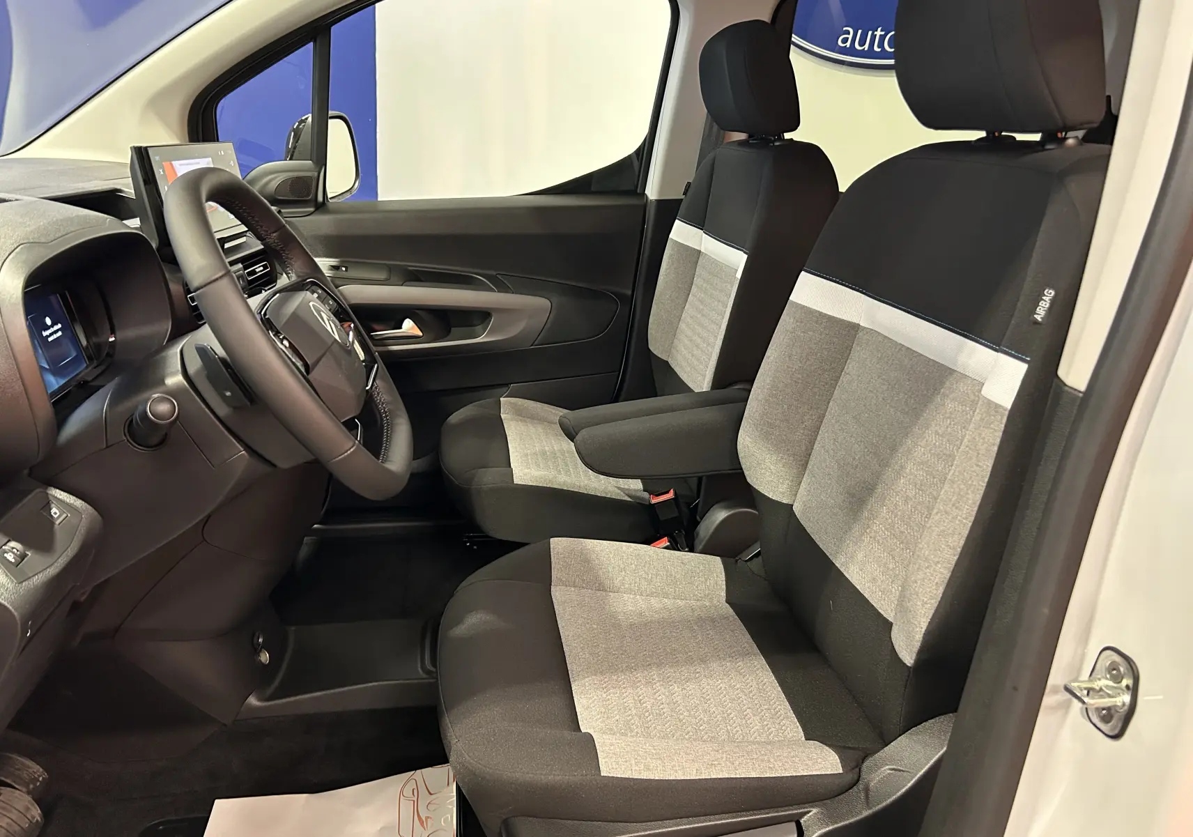 Vue intérieure côté conducteur du Citroën Berlingo Multispace 2026, sièges tissu noir et gris avec accoudoir central.