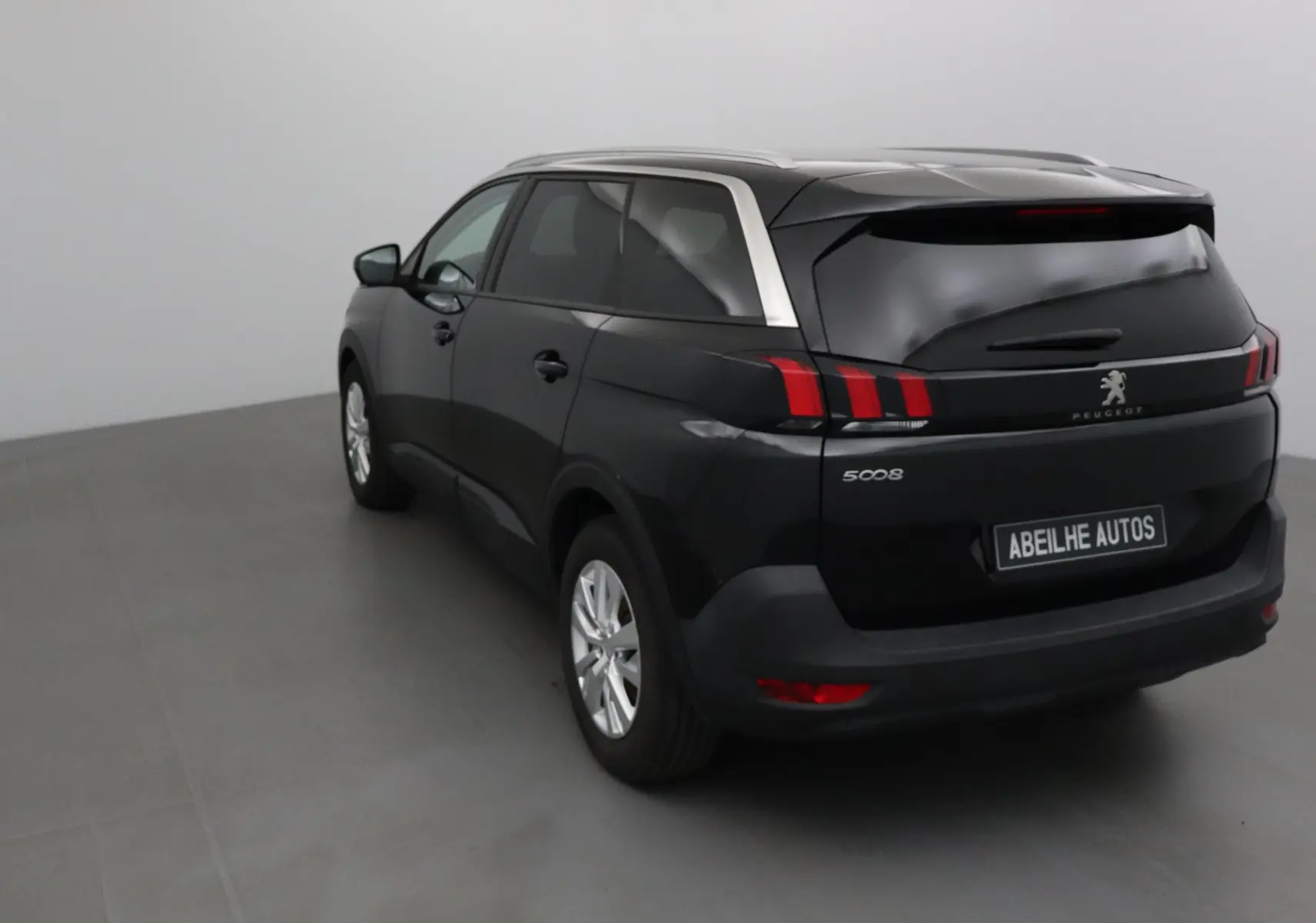 Peugeot 5008 noir vue 3/4 arrière droit, avec barres de toit argentées et feux arrière à griffes rouges.