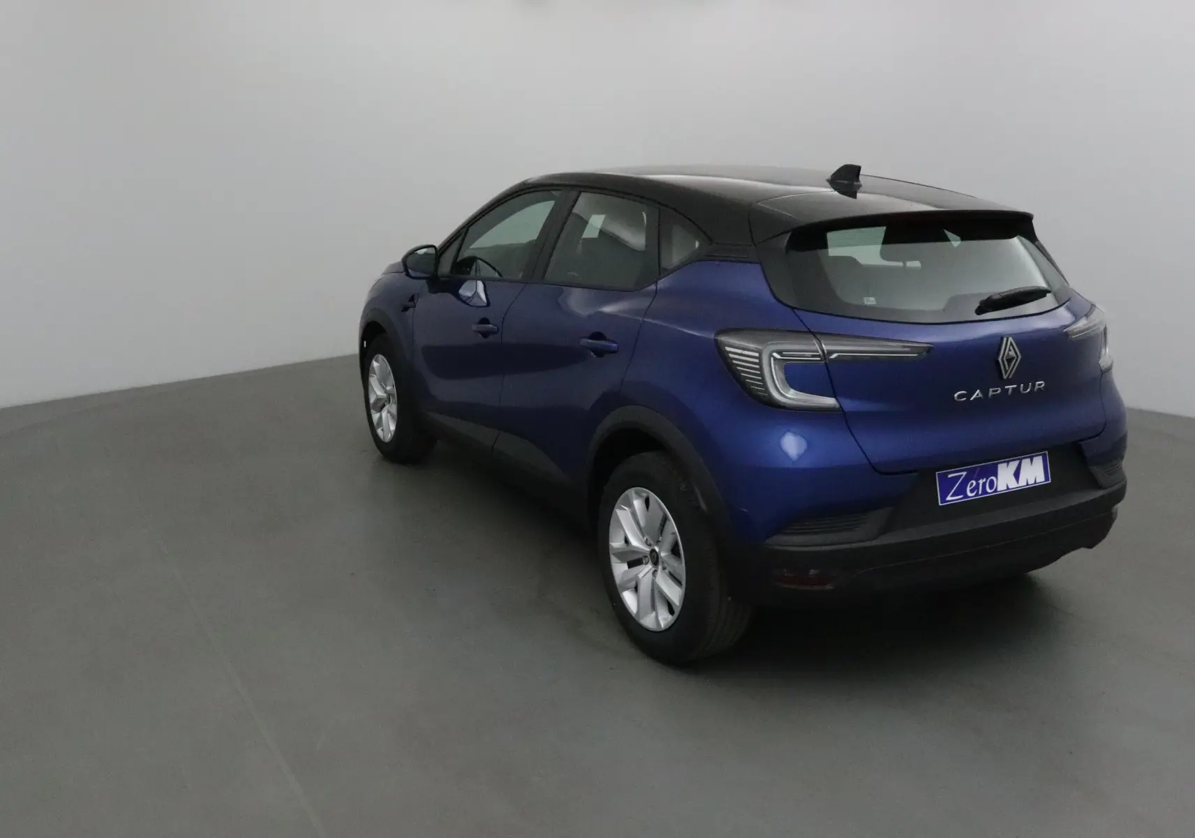Vue 3/4 arrière droite d'un Renault Captur 2025 bleu iron avec toit noir et feux arrière LED distinctifs.