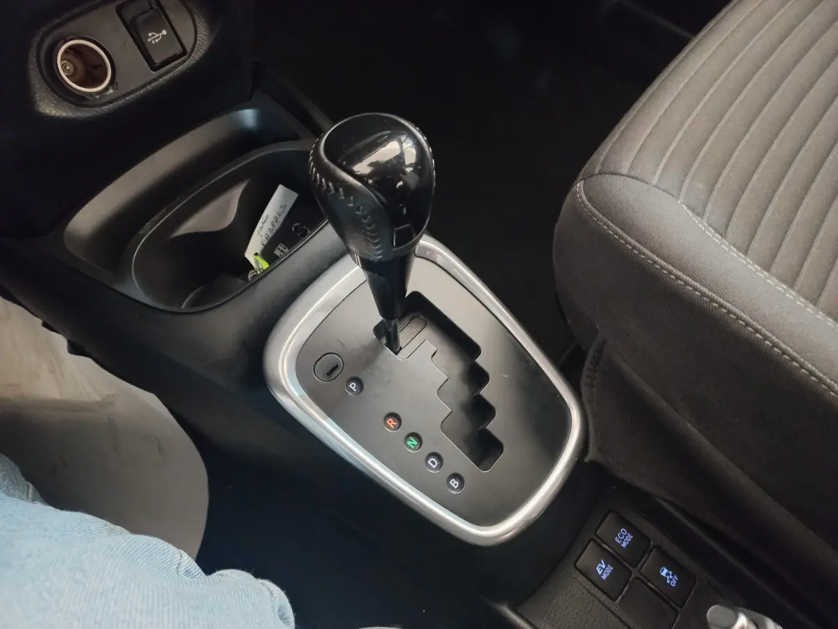 Le levier de vitesse automatique noir vu de dessus dans l'habitacle d'une Toyota Yaris noire, siège tissu gris visible.