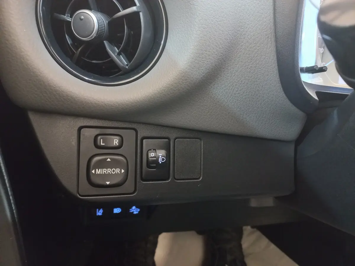 Gros plan sur les commandes de réglage des rétroviseurs et phares côté gauche du tableau de bord noir de la Toyota Yaris hybride 2018.