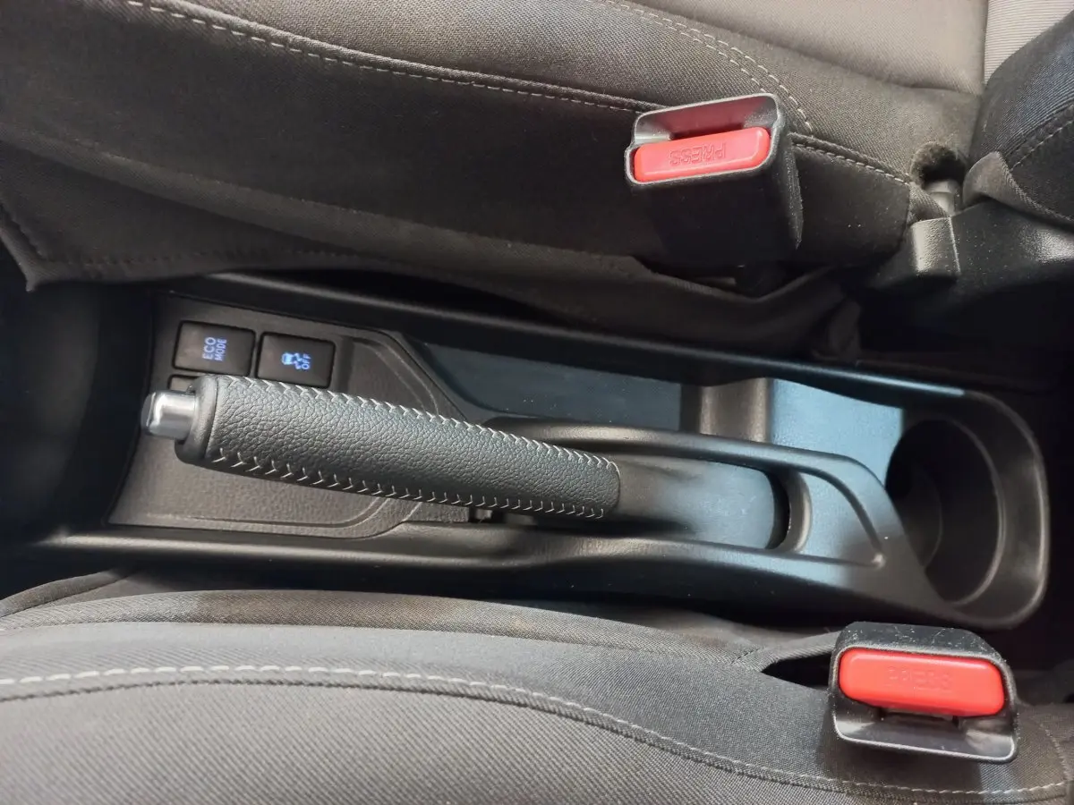 Vue rapprochée de la console centrale noire de la Toyota Yaris 2018, avec frein à main et boutons Eco Mode et traction.