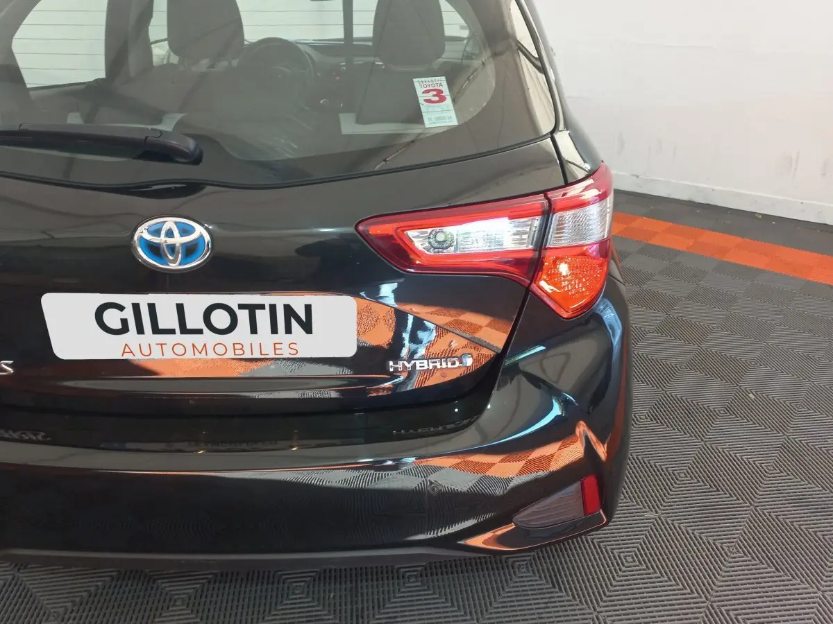 Vue arrière droite d'une Toyota Yaris noire hybride avec logo Toyota et badge Hybrid visible sur le coffre.