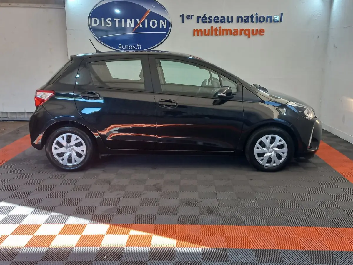 Profil côté gauche d'une Toyota Yaris noire 2018 en hybride, stationnée dans un showroom avec sol à damiers.