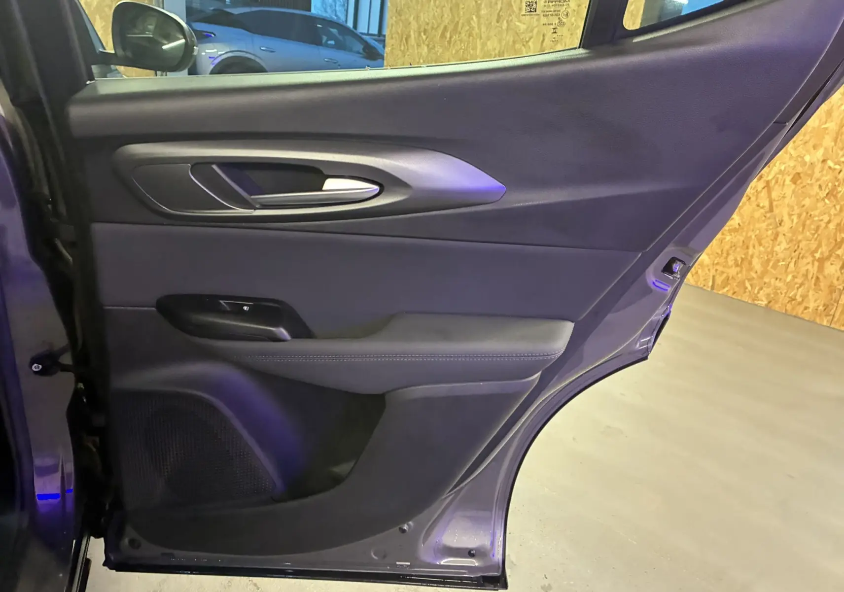 Vue intérieure de la porte arrière droite de l'Alfa Romeo Tonale gris foncé, avec garniture noire et poignée argentée.