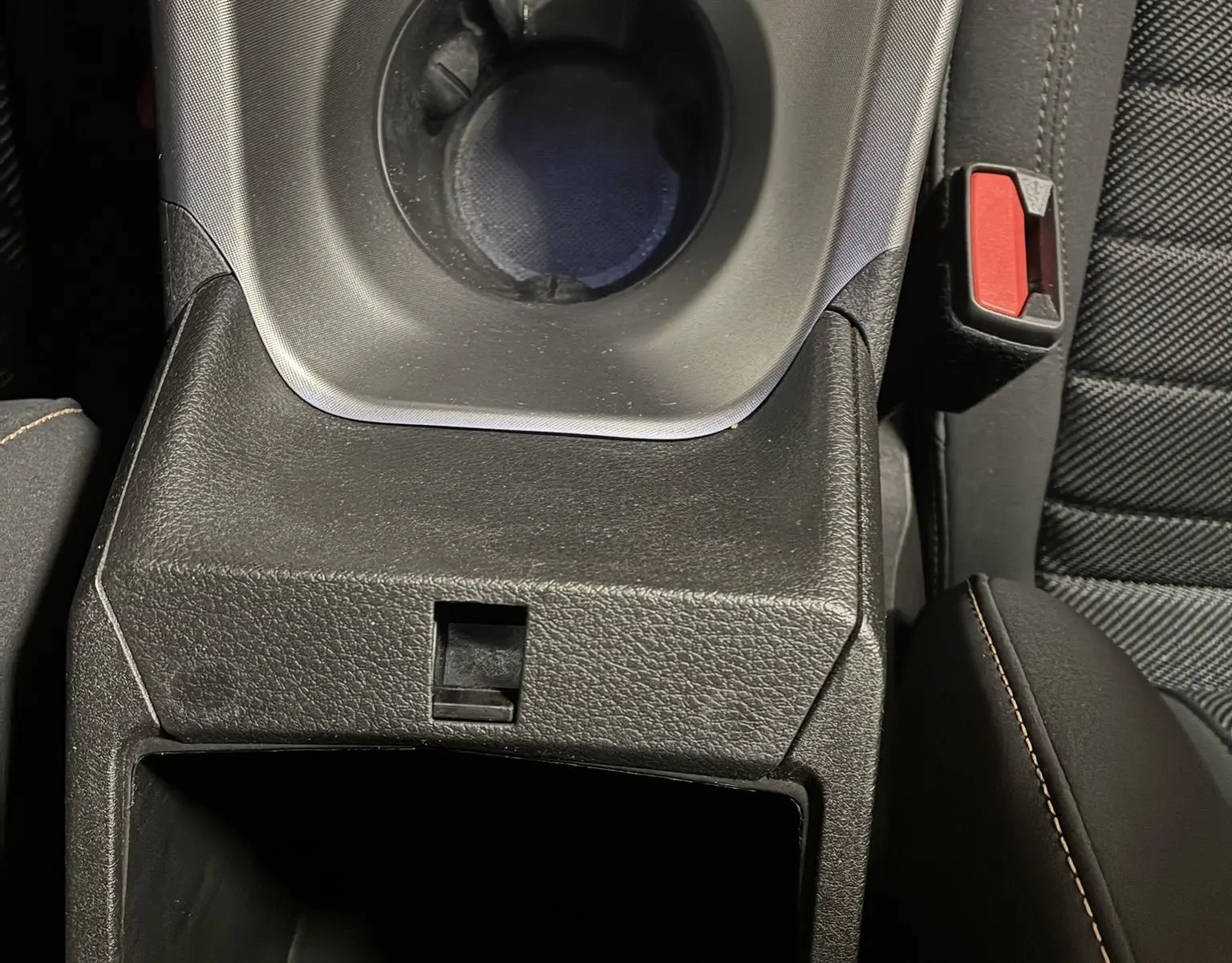 Gros plan sur la console centrale noire de l'Alfa Romeo Tonale 1.3 PHEV avec porte-gobelets et accoudoir en cuir noir.