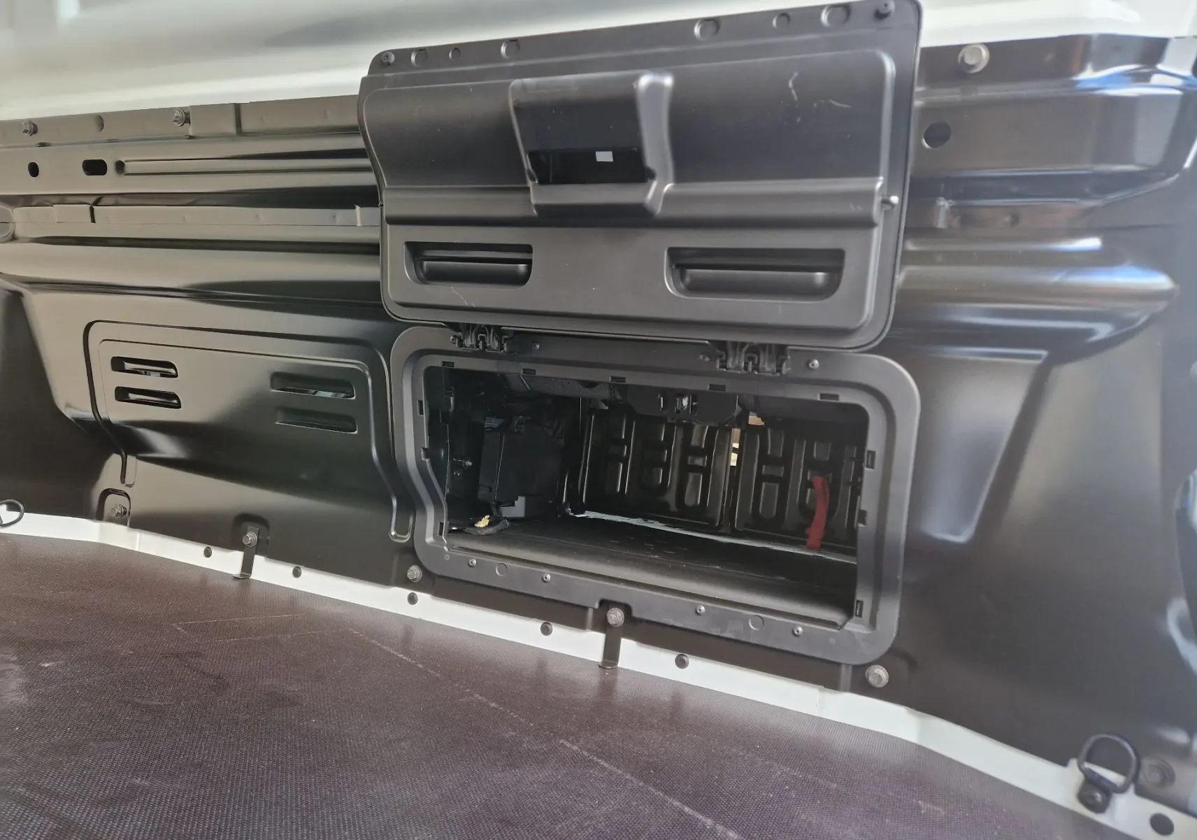 Détail du compartiment de rangement ouvert dans la cloison intérieure noire du coffre du Nissan Primastar blanc.