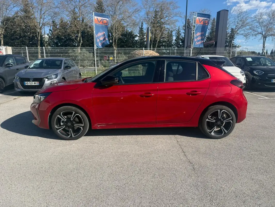Vue latérale côté gauche d'une Opel Corsa rouge 2025 avec jantes noires et toit noir en concession.