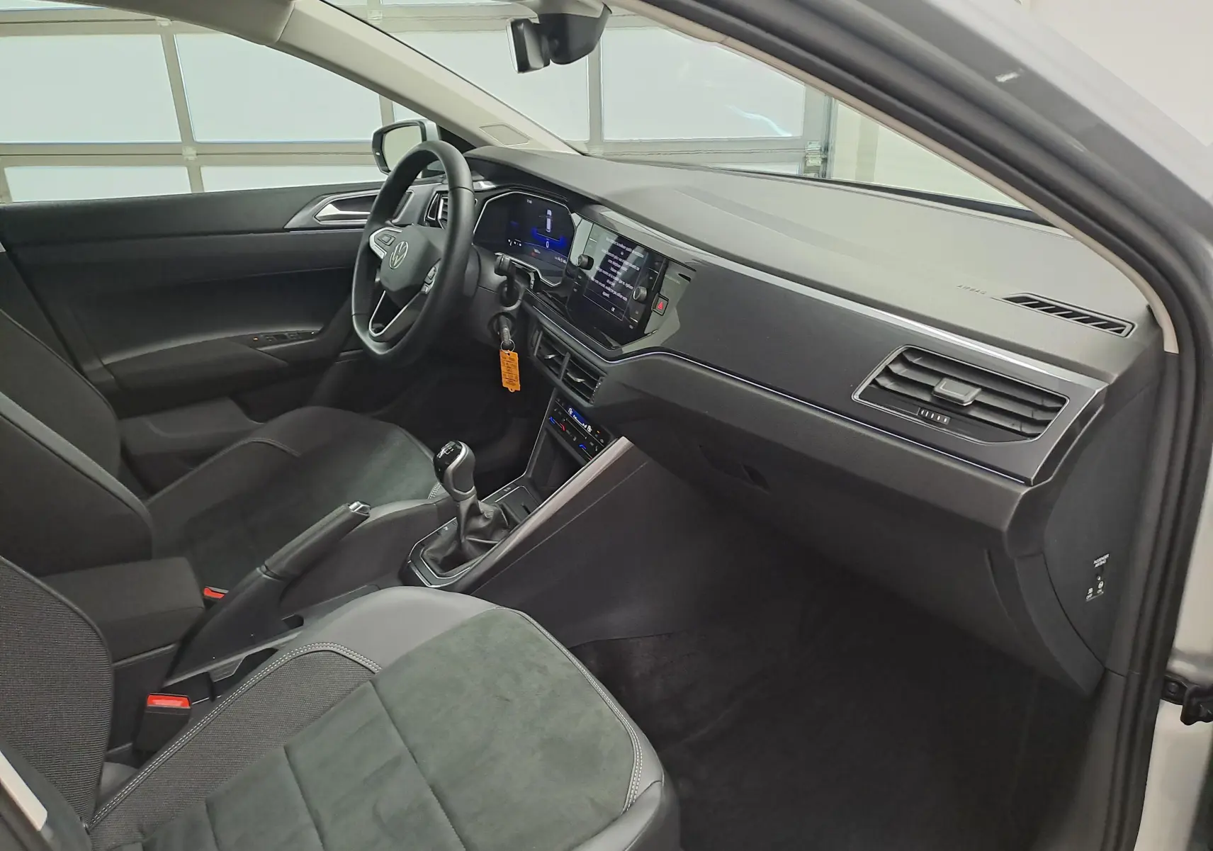 Intérieur de la Volkswagen Polo 2025 en reflet d'argent, vue côté conducteur montrant tableau de bord et boîte manuelle.