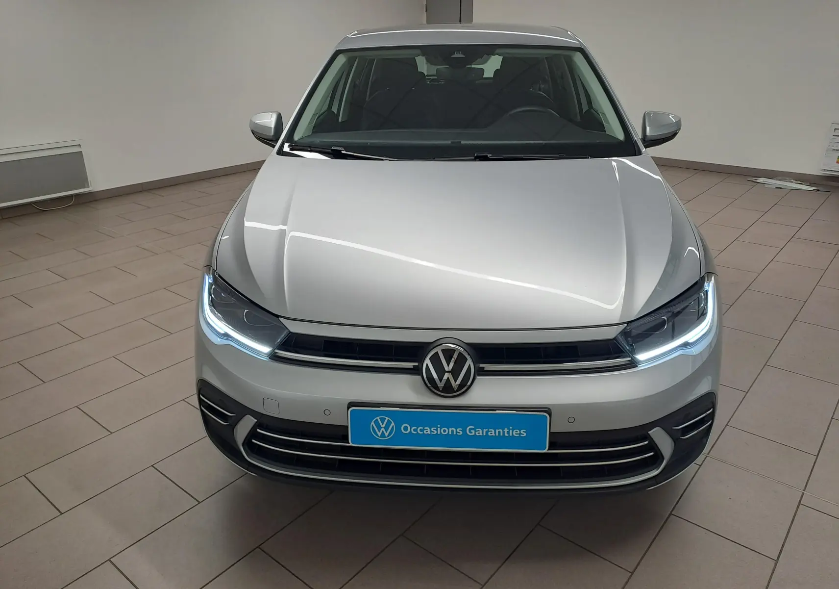 Vue avant d'une Volkswagen Polo 2025 couleur reflet d'argent avec feux LED allumés dans un showroom.