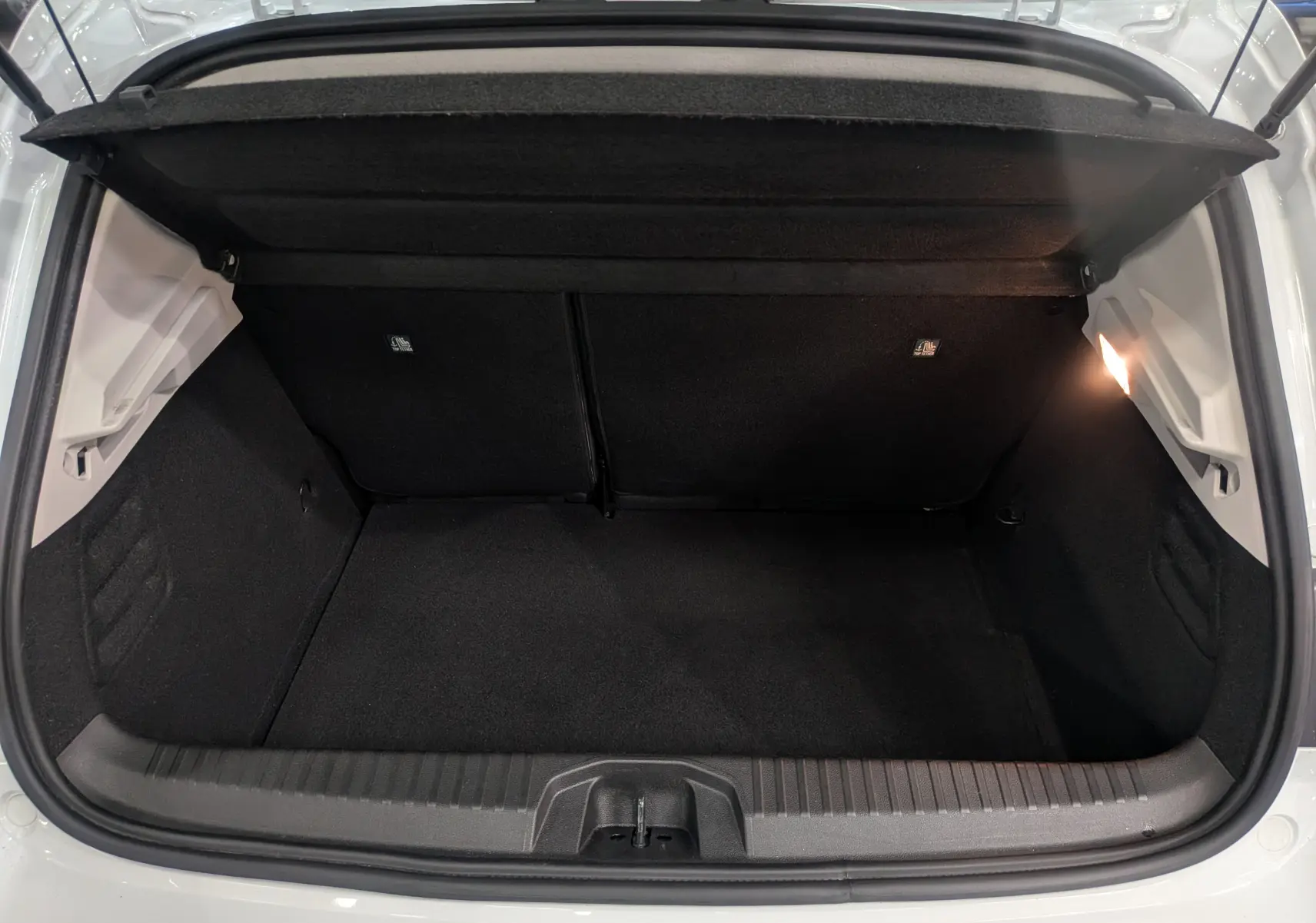 Coffre ouvert vu de l'arrière d'une Renault Clio V blanc glacier, montrant l'espace de rangement vide et éclairé.
