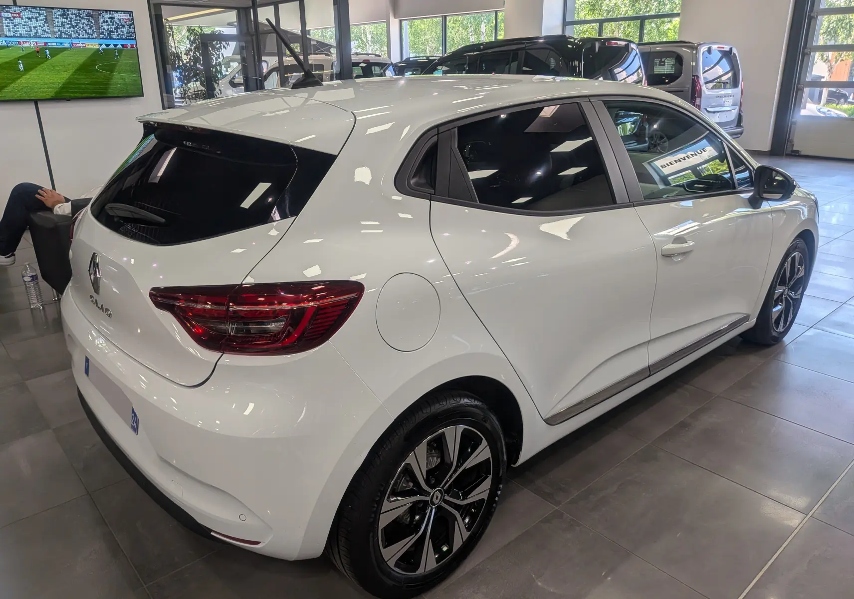 Renault Clio V blanc glacier vue 3/4 arrière droit en intérieur, jantes alliage bicolores et vitres teintées.