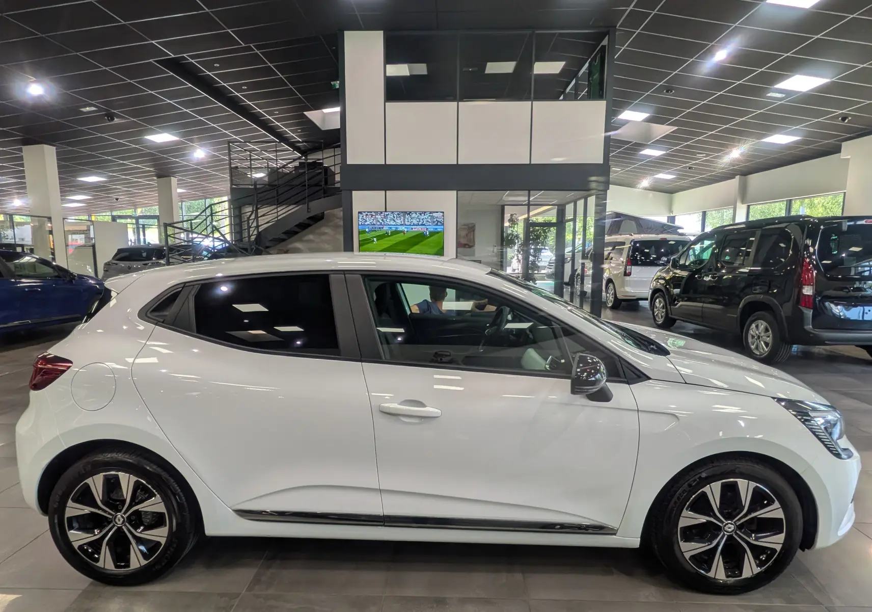 Renault Clio V TCe 100 CH GPL blanc glacier vue de profil côté gauche en intérieur avec jantes alliage bicolores.