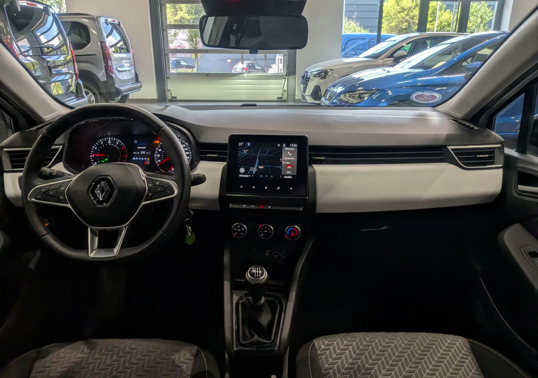 Vue intérieure avant de la Renault Clio V blanche, tableau de bord avec écran tactile et volant multifonction.