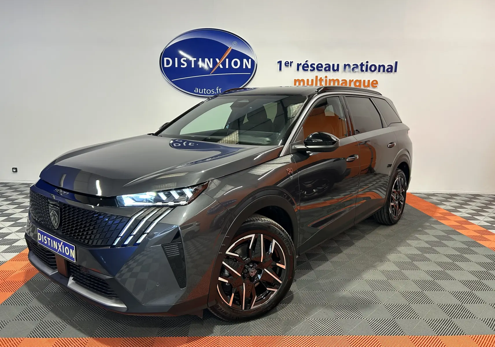 Peugeot 5008 Hybrid gris titane en 3/4 avant droit, avec jantes noires et phares LED allumés.