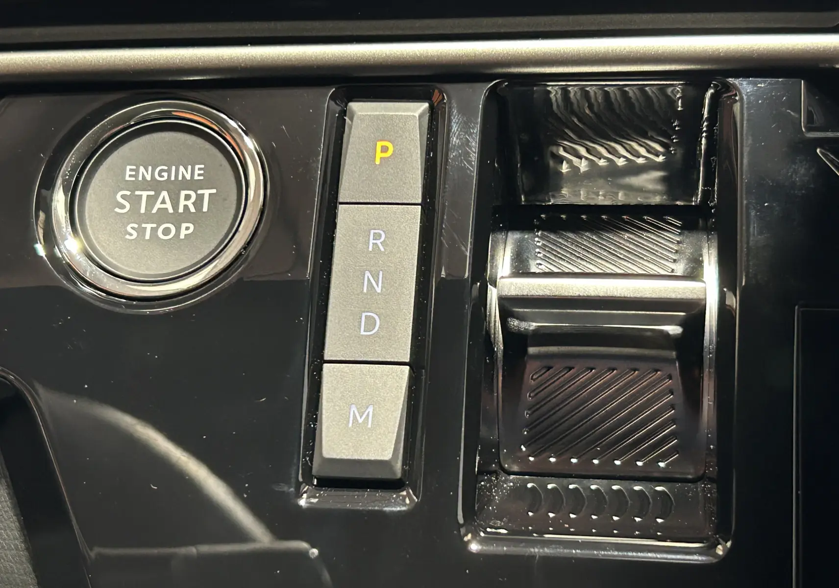 Gros plan sur la console centrale noire du Peugeot 5008 Hybrid avec bouton start/stop et sélecteur de vitesses automatique.