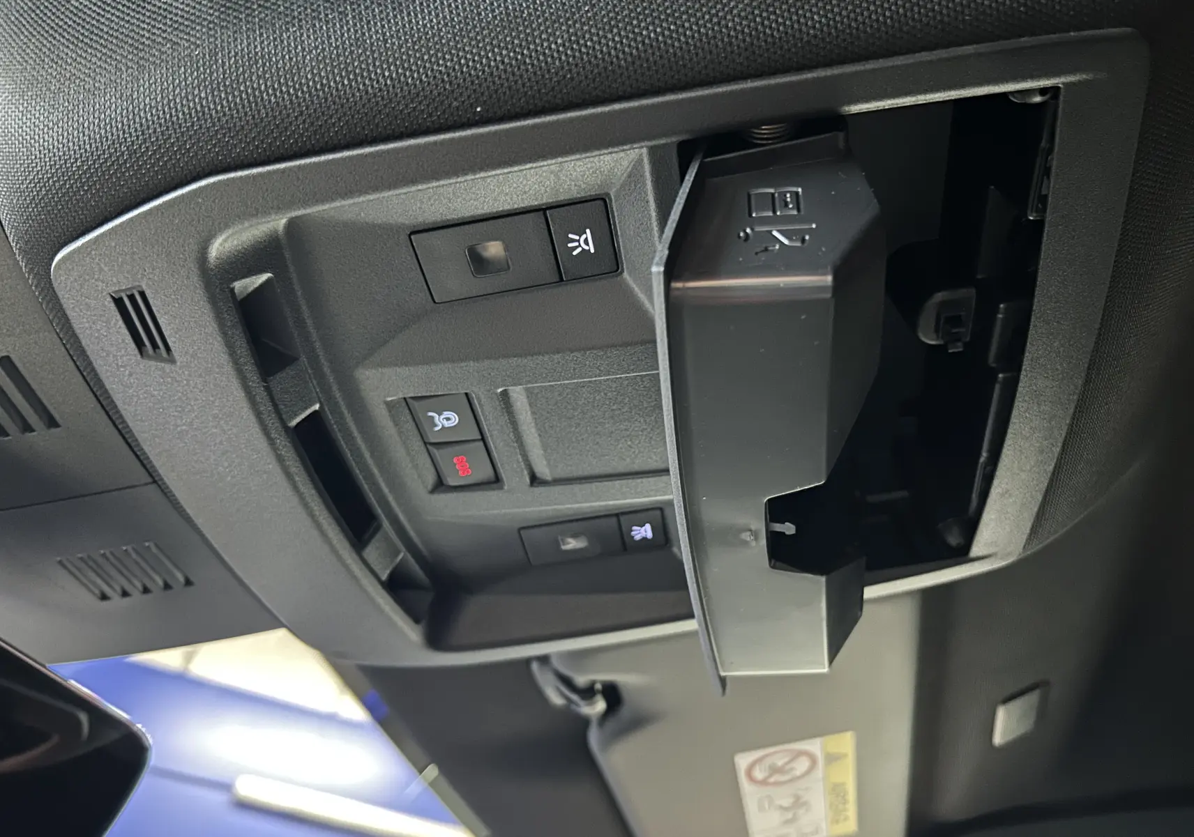 Vue intérieure en gros plan du plafonnier noir avec commandes et compartiment ouvert dans un Peugeot 5008 gris titane.