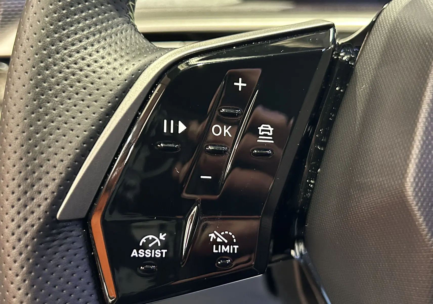 Gros plan sur les commandes noires au volant du Peugeot 5008 Hybrid gris titane, avec boutons de régulateur et assistant.
