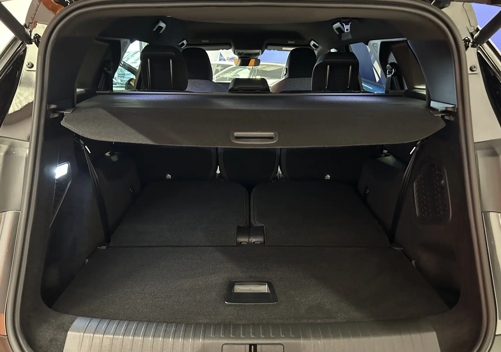 Vue arrière du coffre ouvert du Peugeot 5008 gris titane, avec banquette arrière rabattue et cache-bagages déployé.