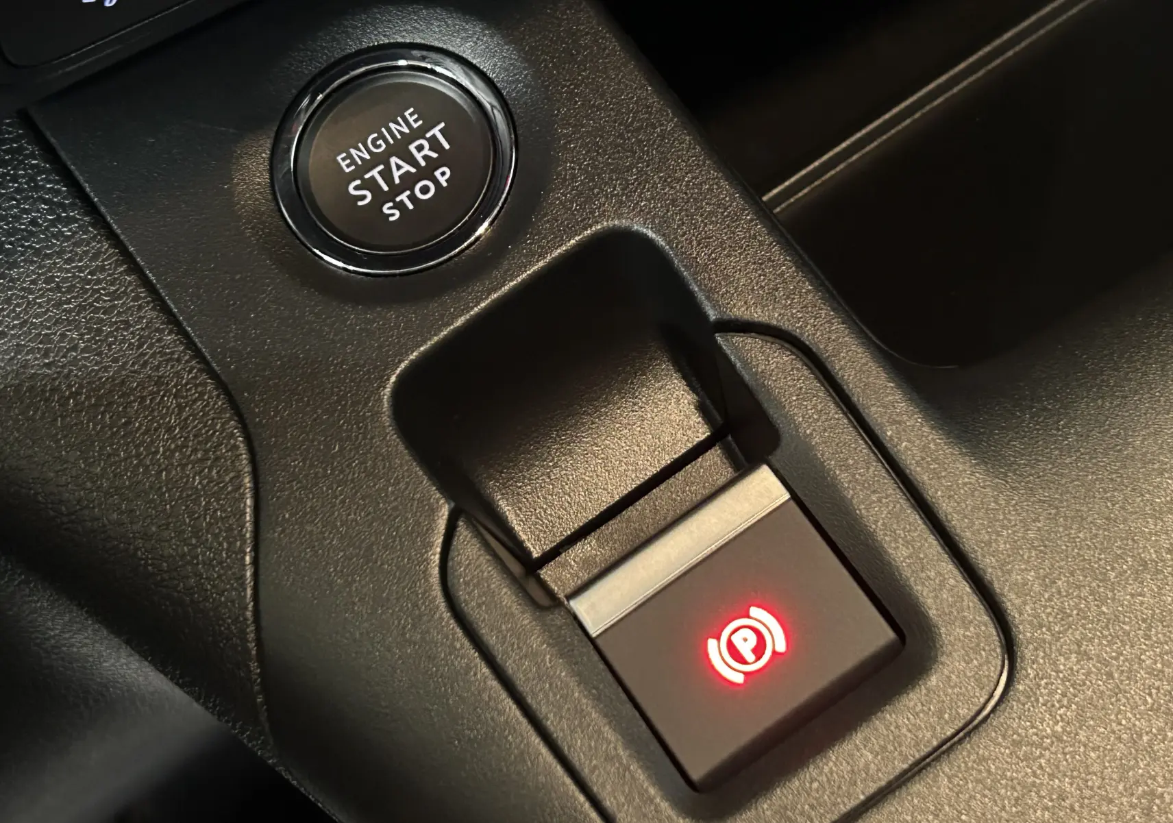 Gros plan sur le bouton de démarrage et le frein à main électrique rouge du tableau de bord noir du Citroën Berlingo Multispace.