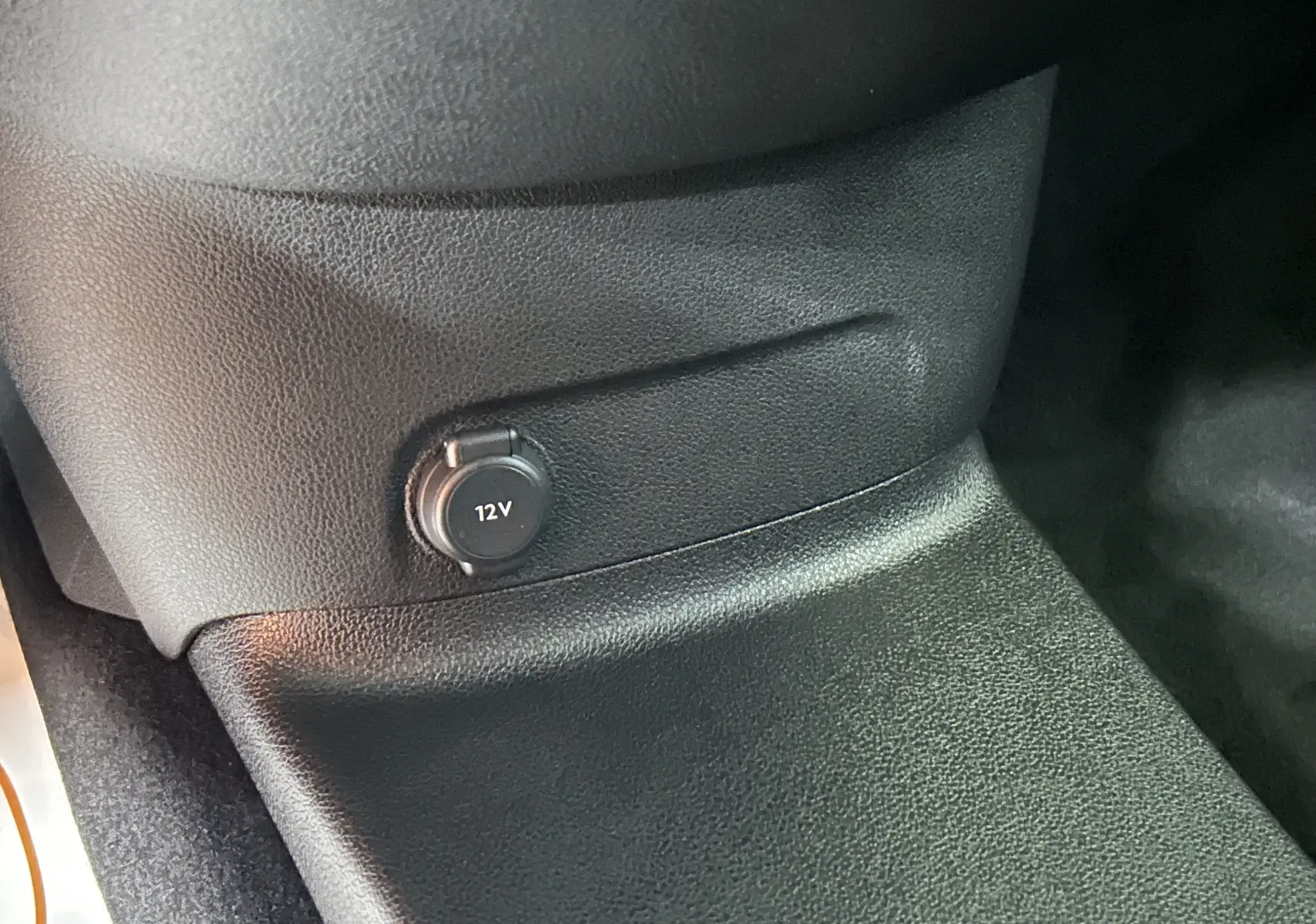 Prise 12V en gros plan sur la console centrale noire du Citroën Berlingo Multispace 2026, intérieur sombre.